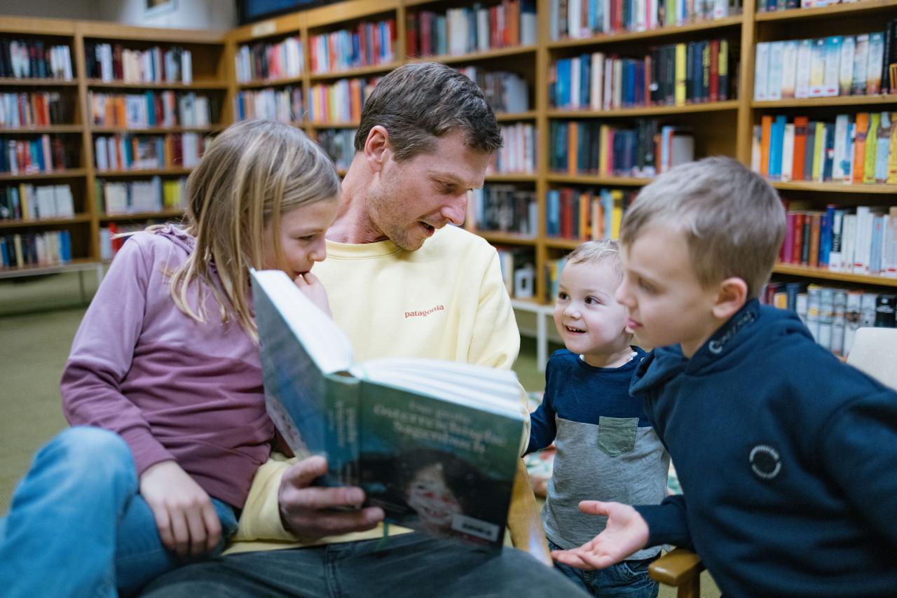 Symbolbild: Vater liest drei kleinen Kindern in der Bücherei vor